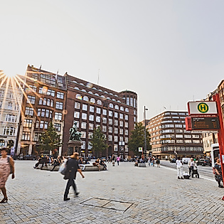 Menschen auf dem sonnigen Gänsemarkt in Hamburg, umgeben von Backsteinfassaden und Geschäften