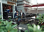 Zwei Personen sitzen im Außenbereich von Playground Coffee, umgeben von Pflanzen und roten Sonnenschirmen