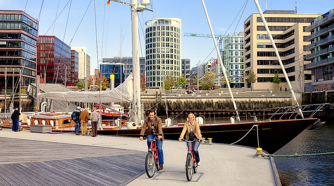 Zwei Radfahrende am Sandtorhafen in der HafenCity Hamburg vor historischem Segelschiff und moderner Architektur