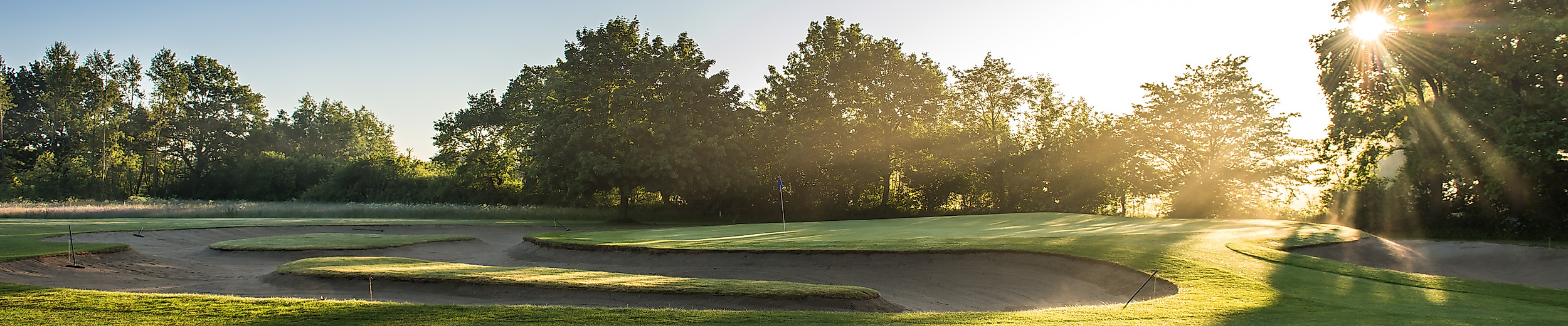 Sonnenbeschienener Fairway im Golf Club Jersbek bei Hamburg mit Bunker und umrahmenden Bäumen