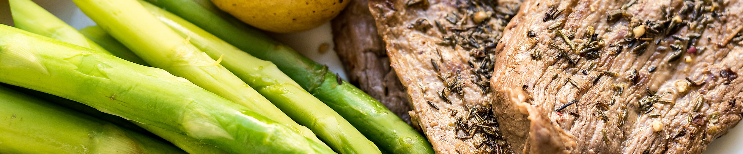 Teller mit grünem Spargel, Salzkartoffeln, Kräutersteak und Schinken – typisch deutsche Küche