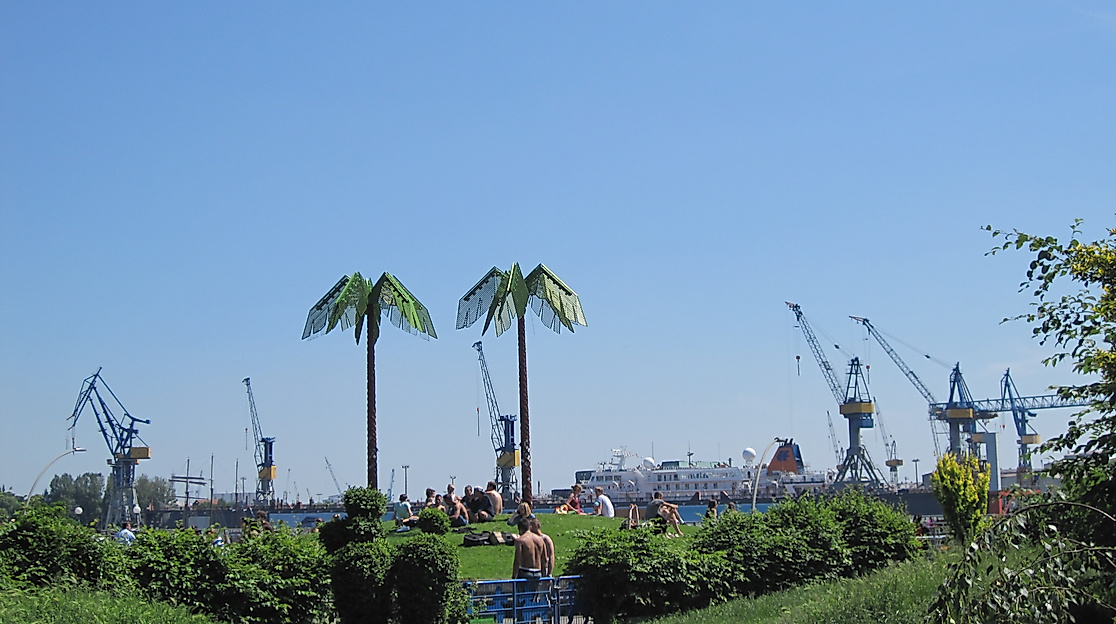 Künstliche Palmen im Park Fiction mit Blick auf den Hamburger Hafen und Hafenkräne bei blauem Himmel