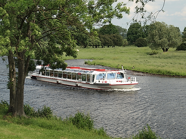 Weißes Alsterschiff der ATG auf ruhigem Gewässer mit grüner Uferlandschaft im Frühling