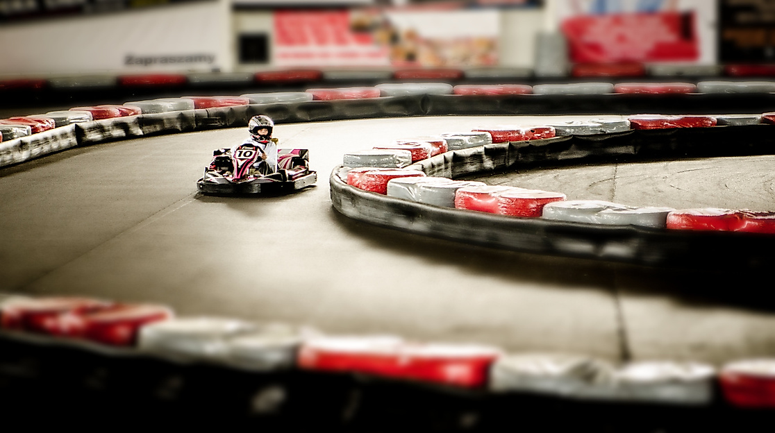 Fahrer lenkt Go-Kart durch eine Indoor-Kurve auf einer Rennstrecke mit rot-weißer Streckenbegrenzung