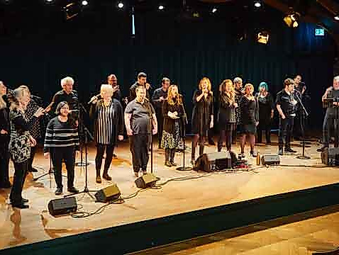 A group of people is standing on a stage, singing together into microphones.