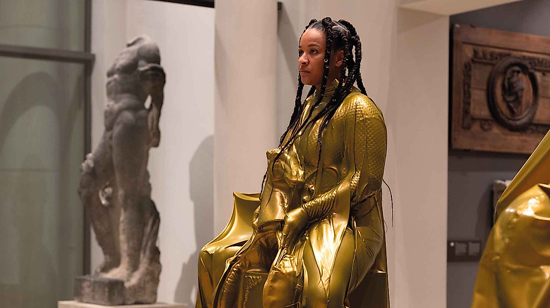 A person wearing a shiny gold-colored suit is on display as an exhibit in the museum.
