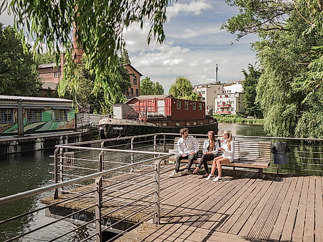 Menschen entspannen an einem Holzsteg am Wasser im alternativen Kultur- und Gartenprojekt Zomia in Wilhelmsburg