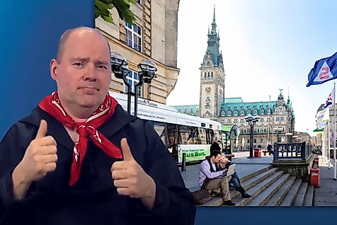 Mann gebärdet vor dem Hamburger Rathaus – barrierefreie Infos zum Nahverkehr.