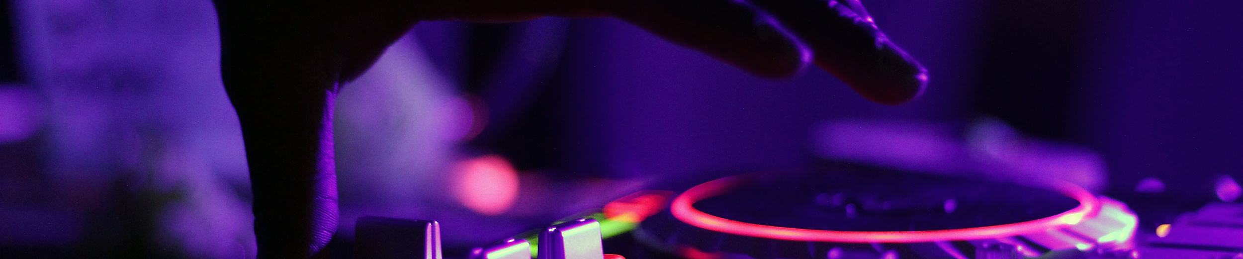 DJ steuert mit Hand ein beleuchtetes Mischpult im Club, violette Lichtstimmung im Hamburger Nachtleben