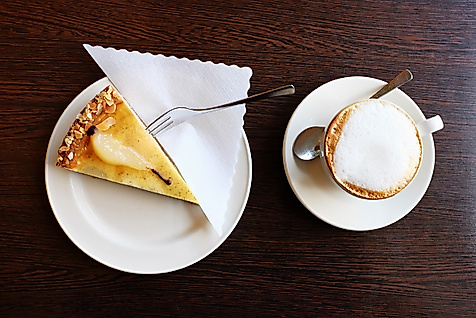 Stück Birnentarte mit Puderzucker und Cappuccino auf Holztisch, serviert in der Biokonditorei Eichel