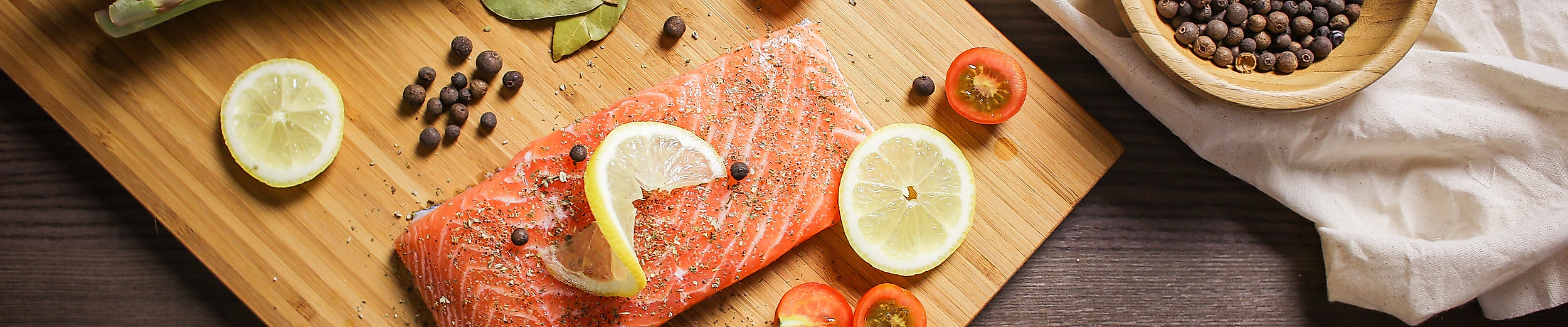 Rohes Lachsfilet mit Zitrone, Gewürzen und Gemüse dekorativ auf Holzbrett angerichtet