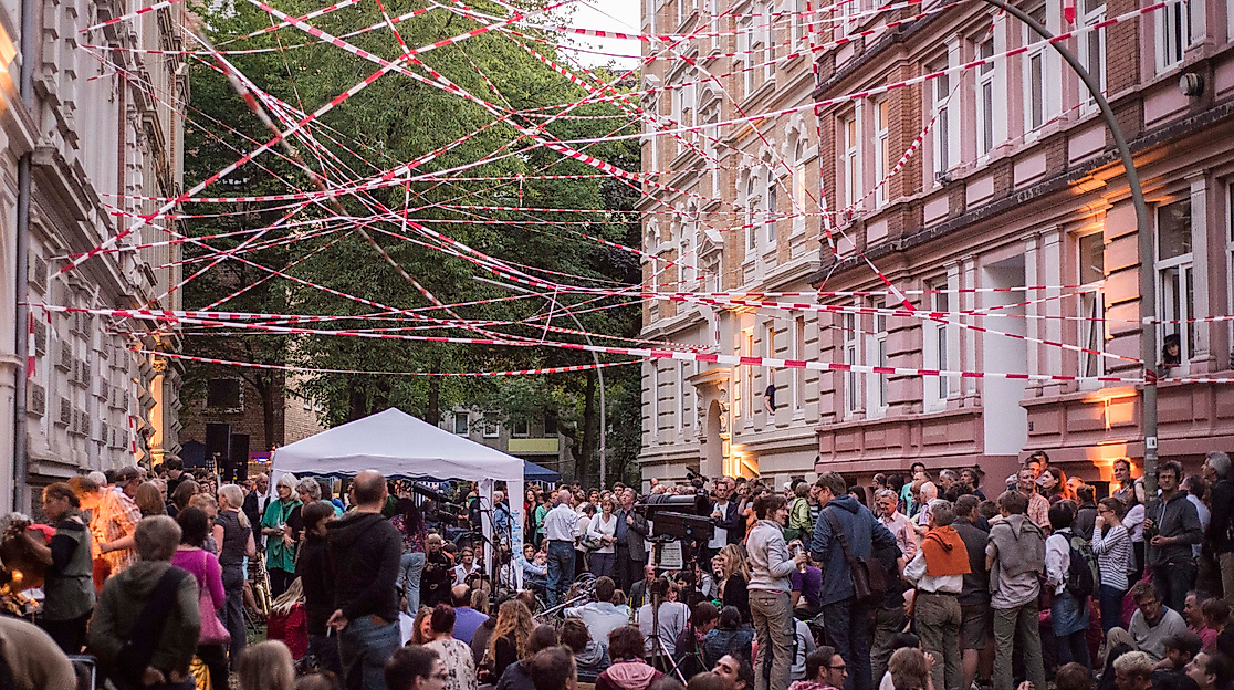 Straßenfest der Altonale in Hamburg mit Menschenmenge, Lichterketten und Bühnenzelt zwischen Altbauten.