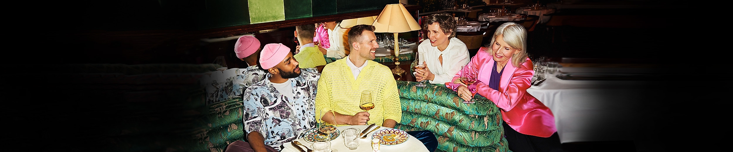 Vier bunt gekleidete Personen sitzen gemeinsam auf einem Sofa in festlich dekorierter Umgebung