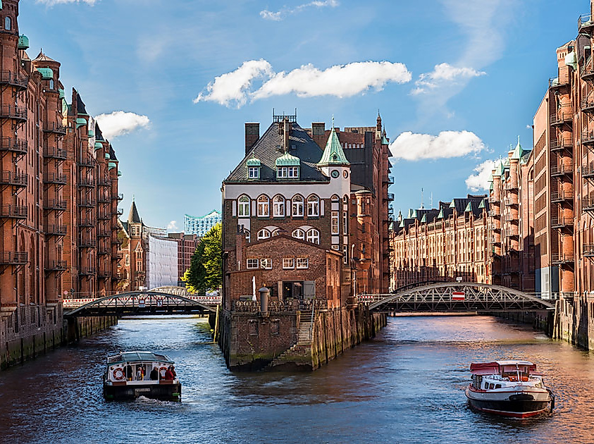 Das Wasserschloss in der Hamburger Speicherstadt zwischen zwei Fleeten bei Sonnenschein, vorn eine Barkasse..