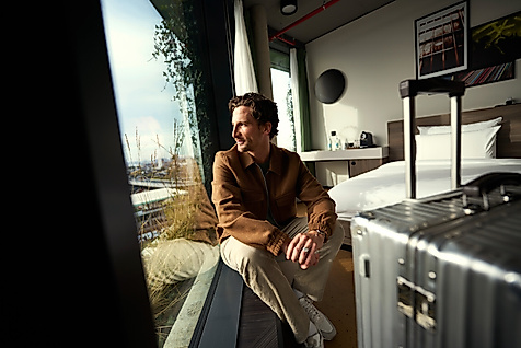 Mann blickt aus dem Fenster eines Hotelzimmers