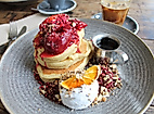 Pancake-Frühstück mit Beeren, Kokoscreme, Orangenscheibe und Ahornsirup auf grauem Teller angerichtet