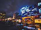 Spielbudenplatz bei Nacht mit beleuchteten Fassaden, Food-Ständen und leuchtender Straßenkunst in Blau und Gelb