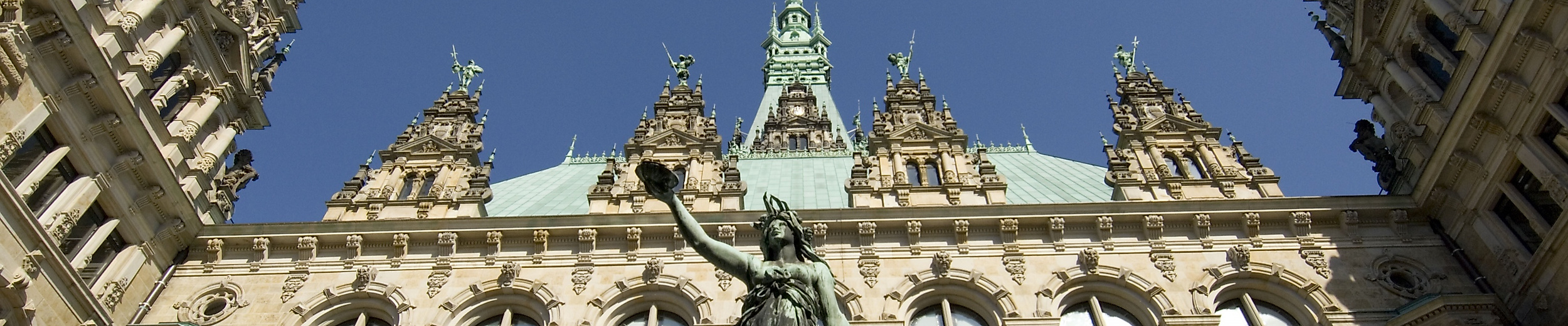 Blick auf die Fassade des Hamburger Rathauses mit Hygieia-Statue vor blauem Himmel
