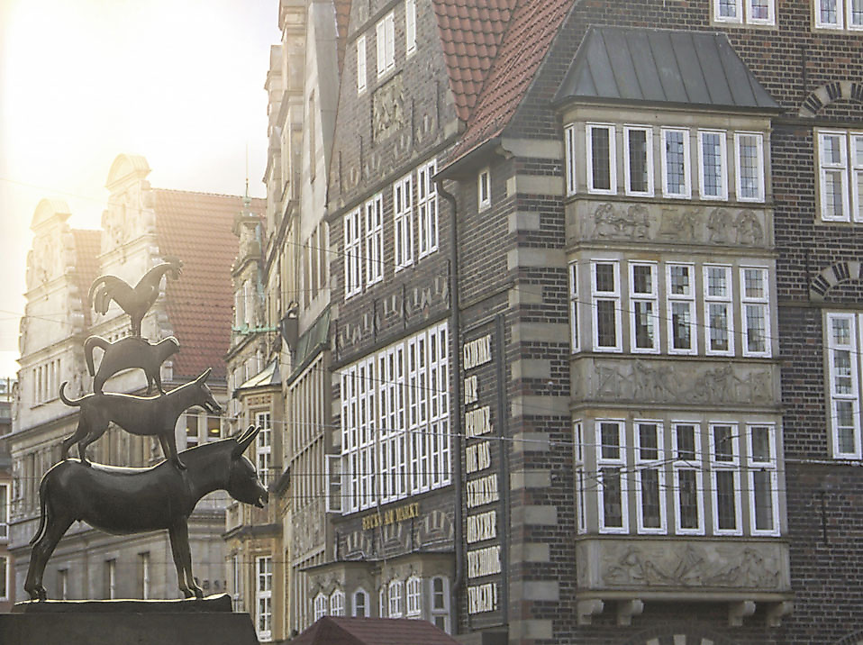 Bronzestatue der Bremer Stadtmusikanten vor historischen Häuserfassaden in der Altstadt bei Sonnenlicht.