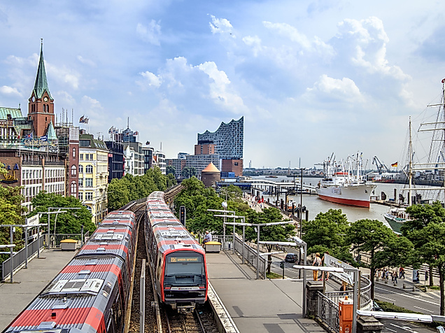 U-Bahn fährt an den St. Pauli Landungsbrücken entlang, im Hintergrund Elbphilharmonie und Museumsschiffe.