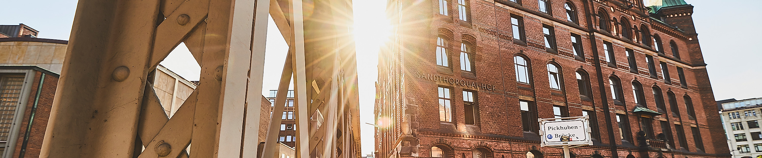 Sonnenlicht fällt durch eine Stahlbrücke auf ein historisches Speichergebäude am Sandtorkai in Hamburg