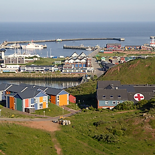Bunte Hummerbuden und Hafenanlage auf Helgoland, umgeben von grünen Hügeln und Nordsee