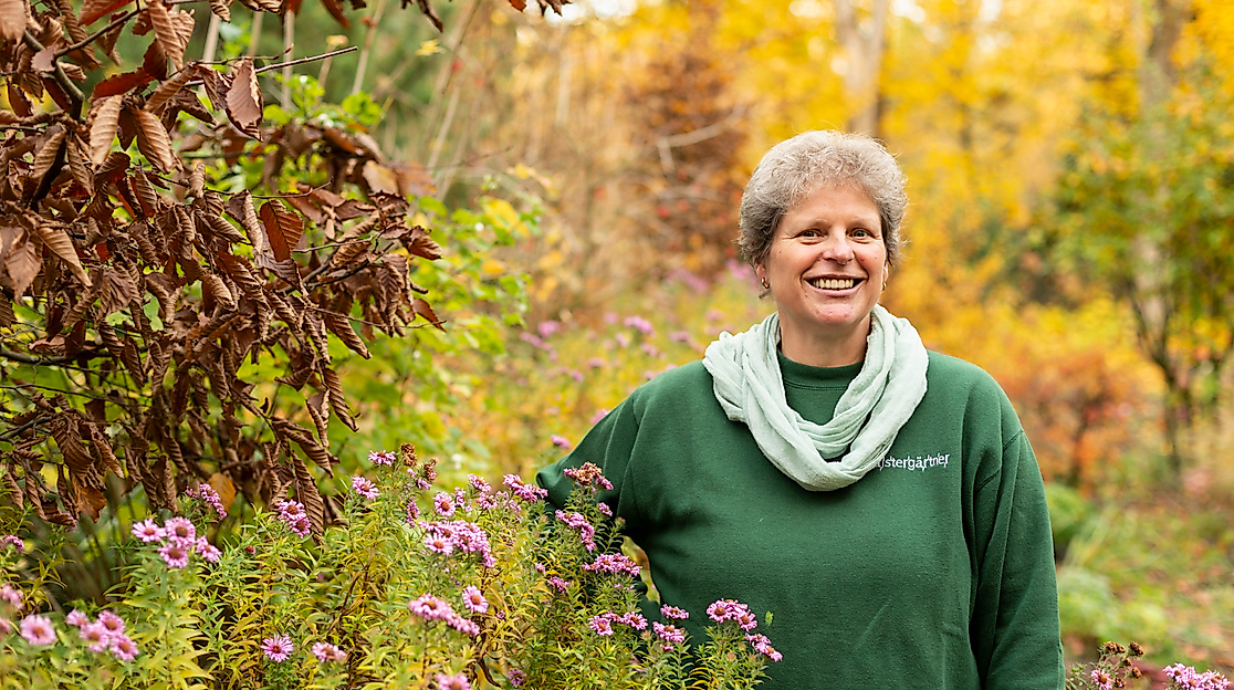 Lächelnde Person im herbstlich blühenden Garten in Hamburg, umgeben von buntem Laub und Wildstauden