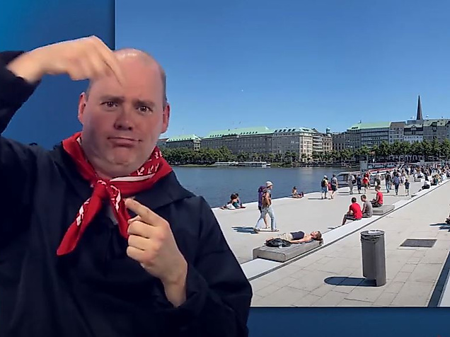 Mann gebärdet vor sonniger Alsterpromenade mit vielen Menschen – barrierefreie Informationen zur Alster in Hamburg.