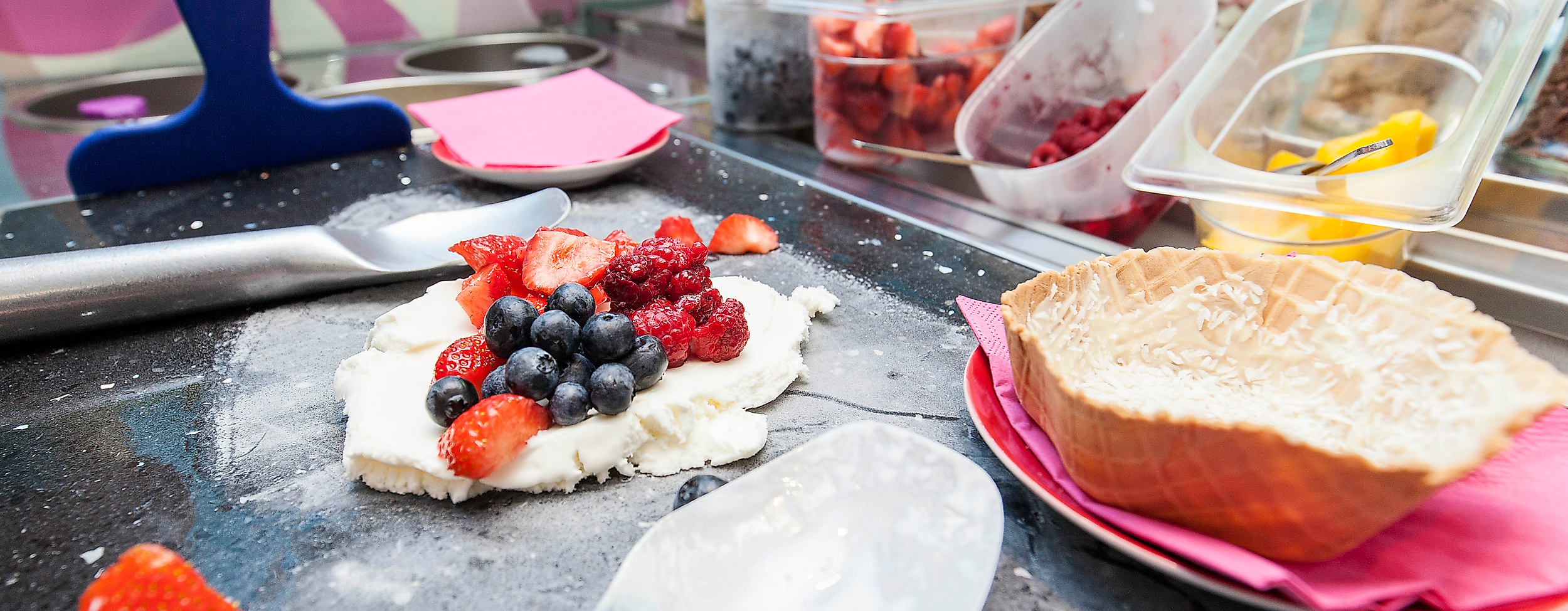Eis wird im Eiscafé Schlecks mit frischen Beeren und Toppings auf einer kalten Platte zubereitet.