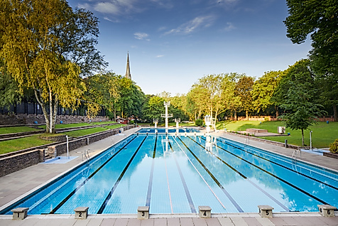 Leeres Schwimmbecken im Sommerfreibad Kaifu, umgeben von Liegewiese und Bäumen bei klarem Himmel