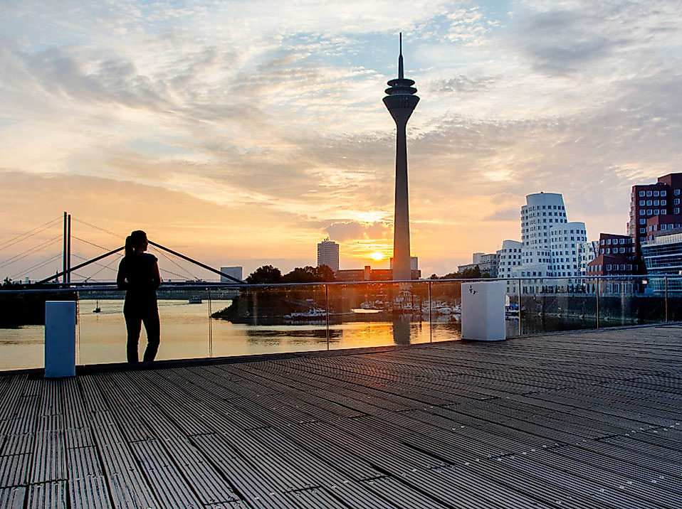 Sonnenuntergang am Rheinufer in Düsseldorf mit Blick auf den Rheinturm und moderne Architektur im Hintergrund.