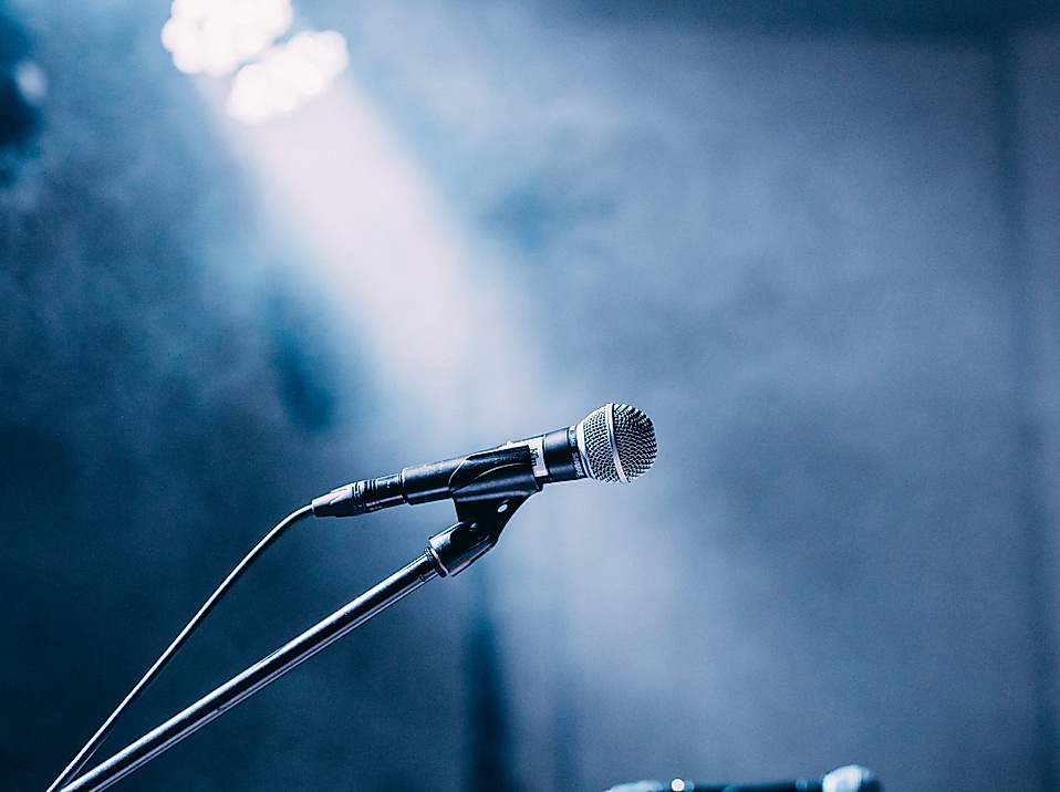 Beleuchtete Mikrofone und Gitarrenhals auf einer dunklen Konzertbühne im Gegenlicht
