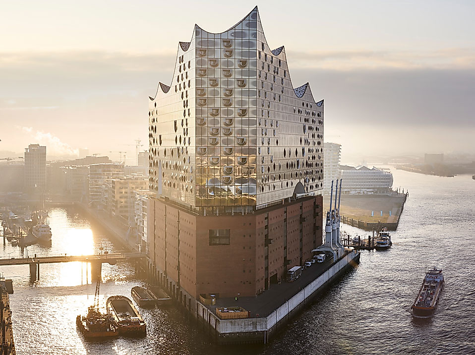  Elbphilharmonie in Hamburg bei Sonnenaufgang, umgeben von Wasser und Schiffen im morgendlichen Licht.