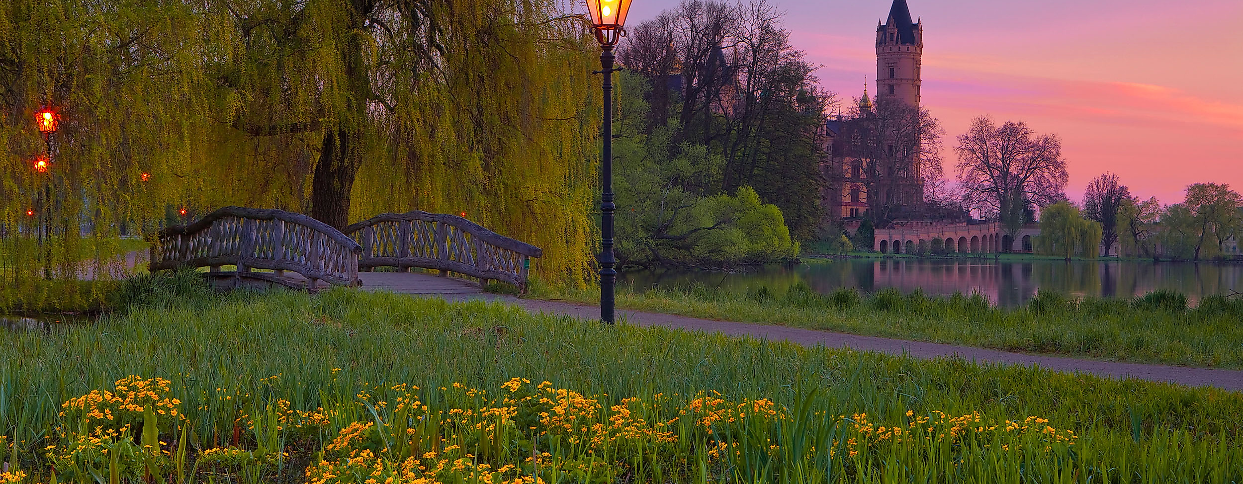 Blühende Schlosswiese mit Laterne im Abendlicht, im Hintergrund das Schweriner Schloss