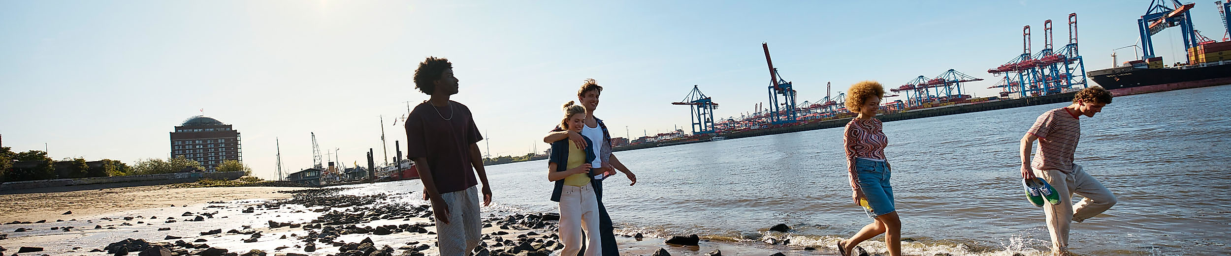 Four young people are taking a walk on the banks of the Elbe under blue skies.