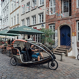 Rikscha fährt durch enge Altstadtgasse mit Außengastronomie und historischen Fassaden in Hamburg