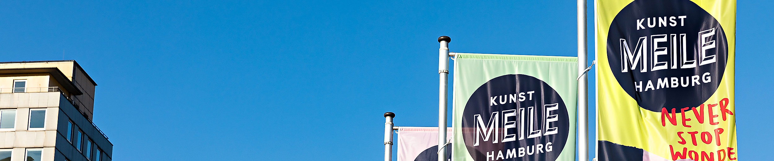 Bunte Kunstmeile-Fahnen mit Grafikmotiv vor blauem Himmel am Hamburger Glockengießerwall