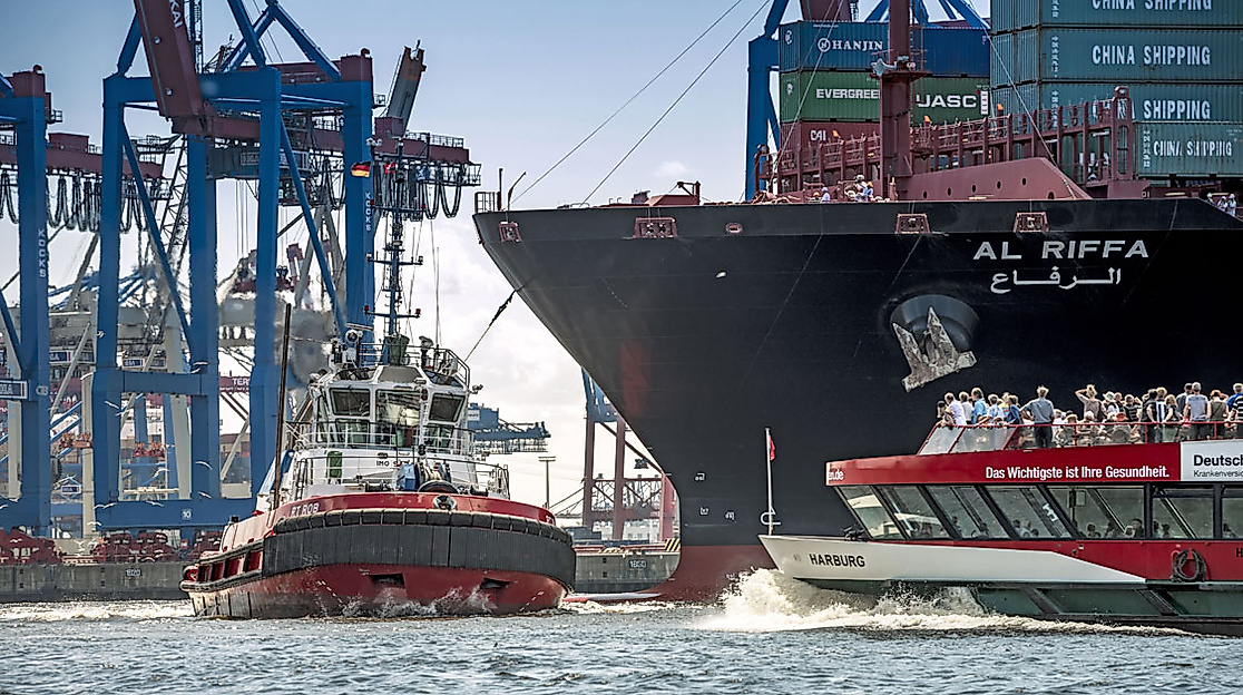 Schiffe vor Containerkränen im Hamburger Hafen bei Sonnenuntergang, mit Hafenschlepper und Ausflugsdampfer auf der Elbe