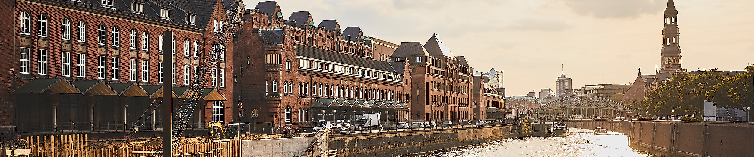 Sonnenlicht spiegelt sich im Fleet der Speicherstadt mit historischen Fassaden und Kirchturm im Hintergrund