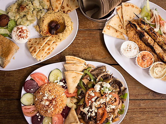 Griechische Spezialitäten wie Gyros, Souvlaki, Tzatziki und Fladenbrot auf drei Tellern serviert.