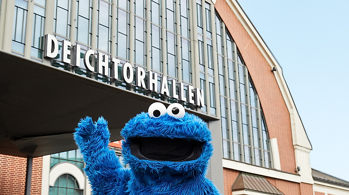 Das Krümelmonster winkt vor dem Eingang der Deichtorhallen Hamburg und wirbt für die Kunstmeile