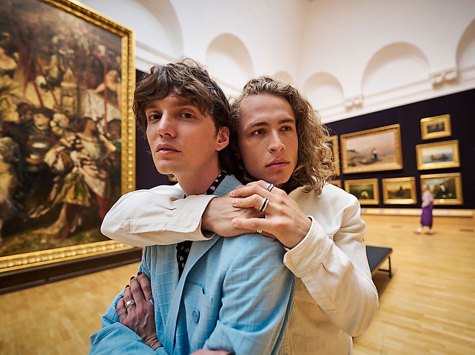 Two young people embrace while standing in a gallery of the Hamburger Kunsthalle surrounded by classical paintings.