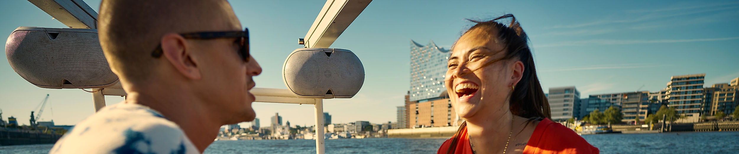 Young people laughing on a boat on the Elbe. The Elphie is in the background.