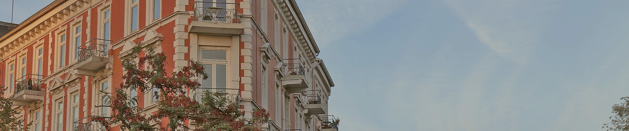 Historisches Gründerzeithaus in Hamburg im Abendlicht, flankiert von blühenden Bäumen und blauem Himmel