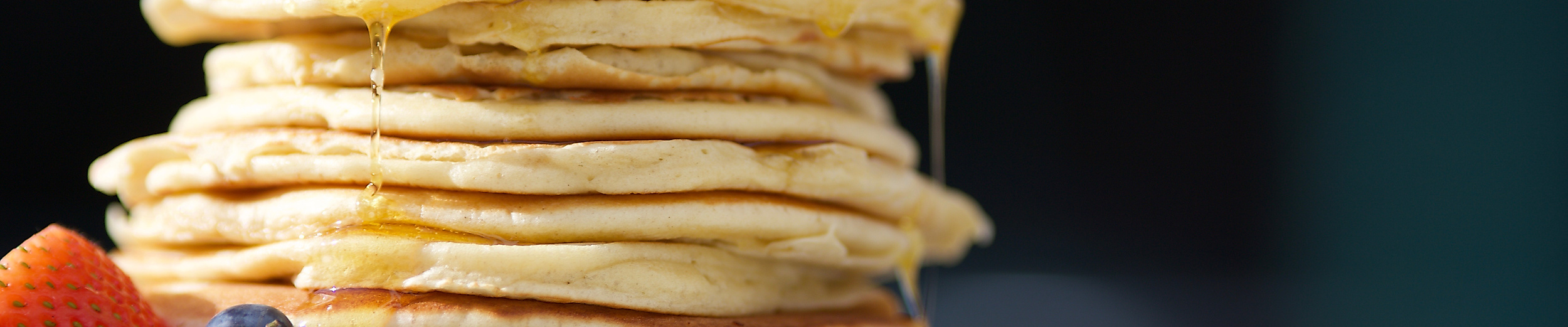 Hoher Stapel Pancakes mit Ahornsirup und Beeren auf weißem Teller appetitlich angerichtet