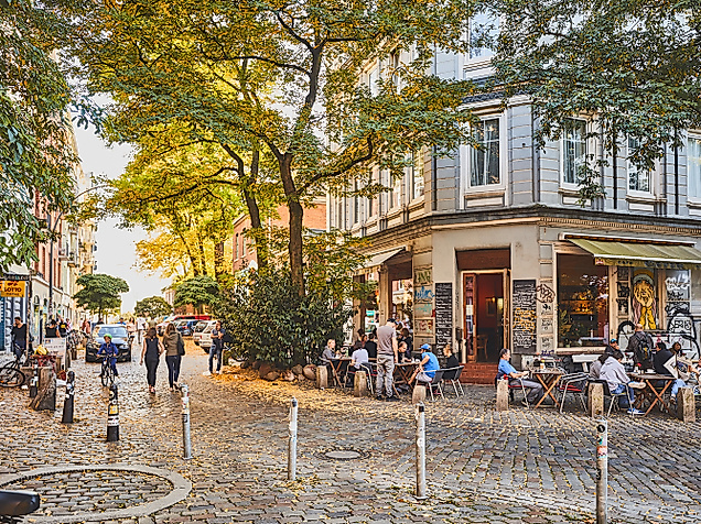 Belebter Hein-Köllisch-Platz in Hamburg mit Straßencafé, Passant:innen und sommerlicher Abendstimmung