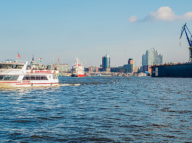 Barkasse auf der Elbe mit Blick auf Hafenkräne und Skyline von Hamburg bei Sonnenschein.