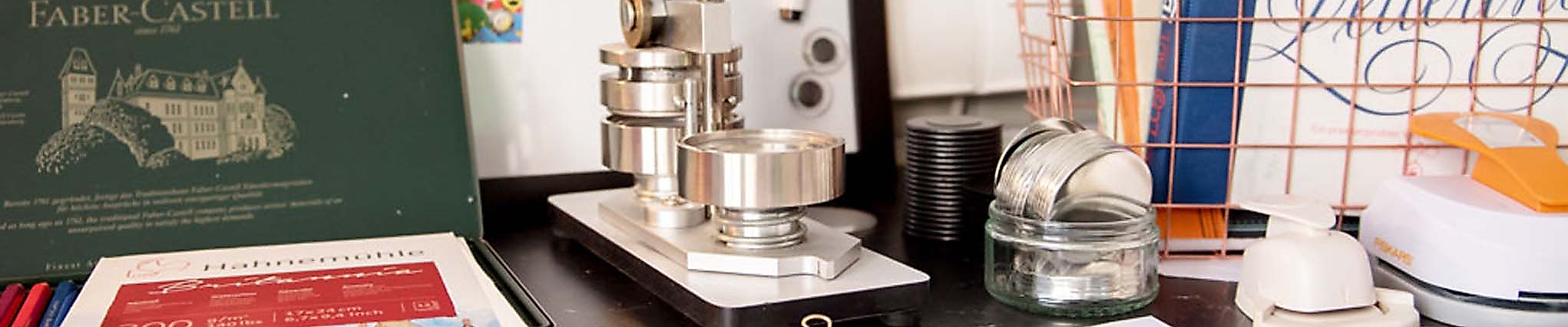 Lettering-Arbeitsplatz mit Papier, Stempelpresse, Farben, Schere und Kreativmaterialien auf schwarzem Tisch.