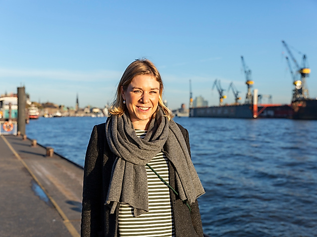 Frau am Hamburger Hafen bei Sonnenschein mit Blick auf die Elbe und Werftkräne im Hintergrund