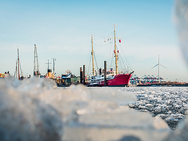 Historische Schiffe im verschneiten Hamburger Museumshafen mit Eisschollen im Vordergrund an einem Wintertag